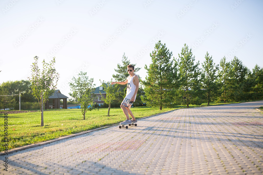 Young skater performing with longboard at sunset in city park. Trendy man having fun with skateboard outdoors, extreme sport concept
