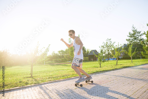 Young skater performing with longboard at sunset in city park. Trendy man having fun with skateboard outdoors, extreme sport concept