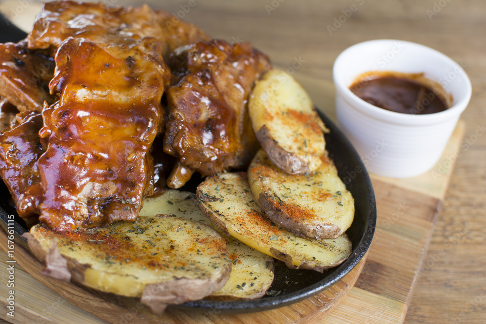 Delicious barbecued ribs seasoned with a spicy basting sauce and served with chopped potato on a wooden chopping board in a restaurant.