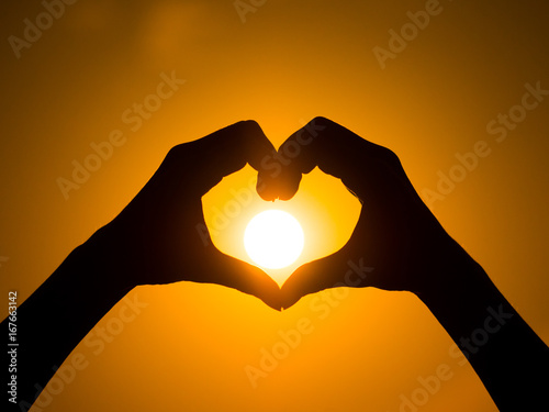 Hand heart frame shape silhouette made against the sun and sky of a sunrise or sunset on a deserted empty beach