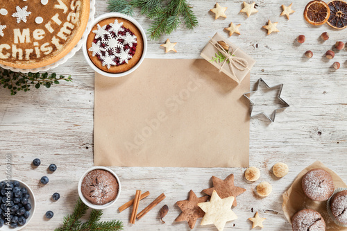 Cooking butter biscuits on a wooden table with Christmass accessories such as snowflakes, sweets, cinnamon, on a beige wooden background. Christmass background with branches of furry spruce. Top view.