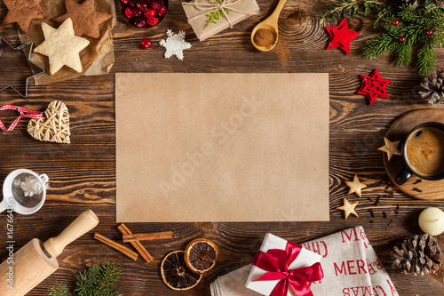 Christmass symbols baking in form of stars, candle, cinnamon and empty piece of paper on center. Christmass background with branches cup of coffee, gift with red ribbon on a wooden background.