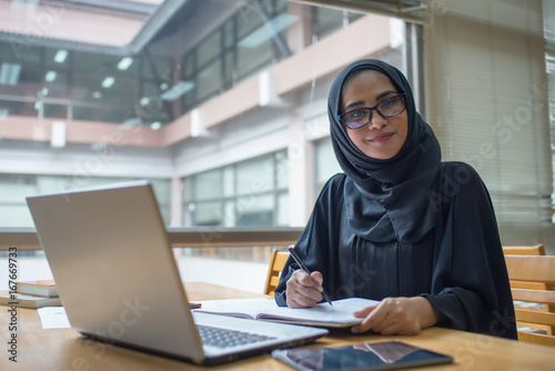 Arabic woman taking notes preparing exam and learning lessons from a book at library.