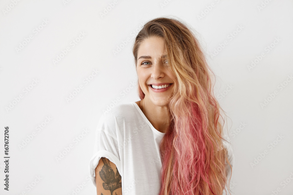 Φωτογραφία Lovely female with pure skin, blue shining eyes and pink hair tips, wearing casual T-shirt, smiling pleasantly into camera while having good mood in morning