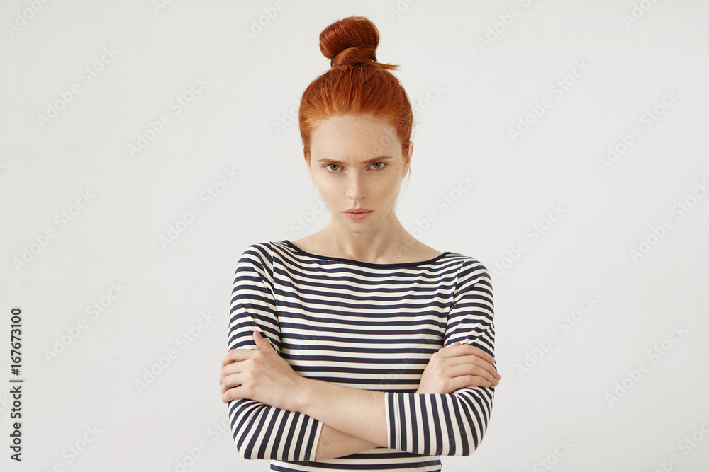 Φωτογραφία Angry ginger female with hair knot, wearing casual clothes, keeping her hands crossed, looking with displeased expression into camera, having quarrel with her boyfriend or parents
