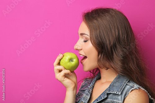 Portrait of young woman with apple on pink background