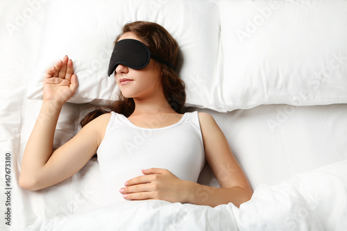 Young woman sleeping with eyemask in white bed photo