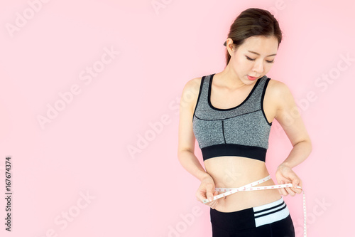 Young asian beautiful woman with sport fitness concept, workout, exercise, measure tape at waist on pink background