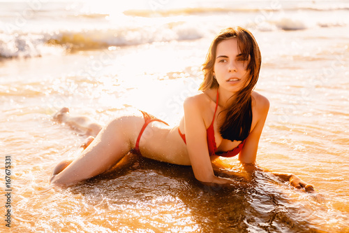 Beautiful slim woman in red bikini relaxed on beach at sea.