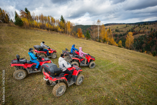 Five ATV riders on off-road quad bikes on the hillside at the background of autumn forest with colorful trees and mountains. Top view