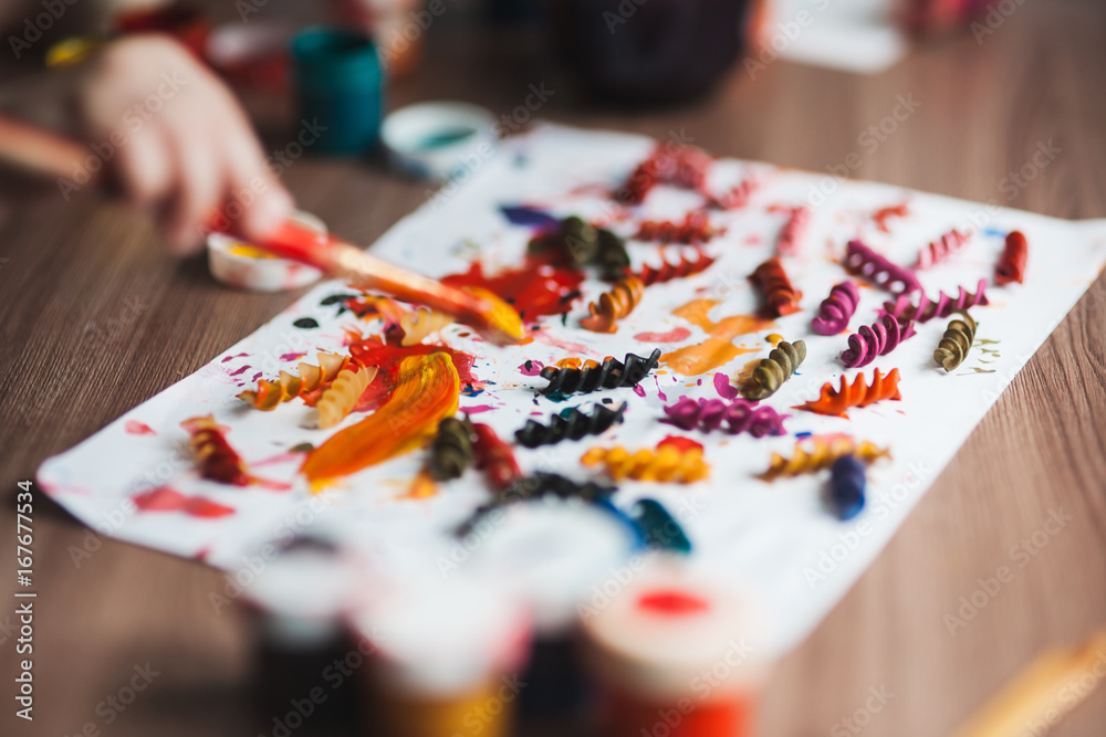 The child is engaged in creativity, decorating pasta with colored paints beautiful background The child is engaged in creativity, decorating pasta with colored paints beautiful background