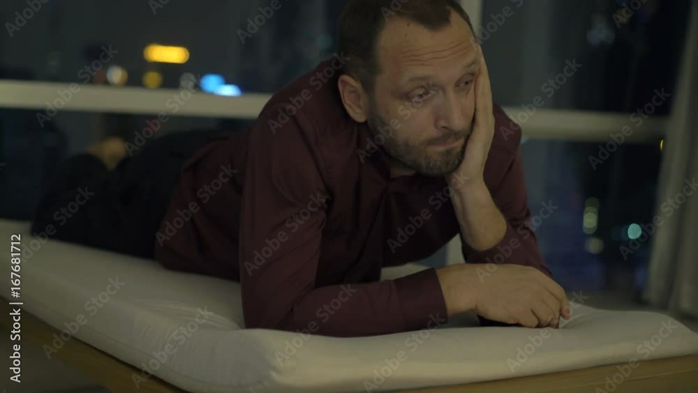 Sad, unhappy man lying on lounger at home at night
Sad, unhappy man lying on lounger at home at night
