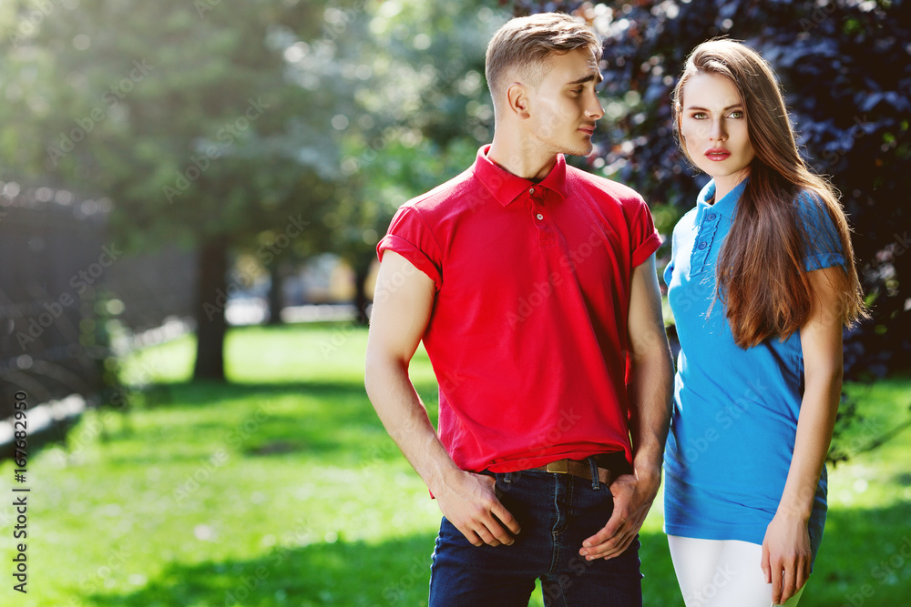 Outdoor portrait of young beautiful fashionable couple. Man and woman  posing in park. Models wearing stylish sport clothes, polo shirts. Sunny day  light. Fashion, lifestyle concept. Copy, empty space Stock Photo