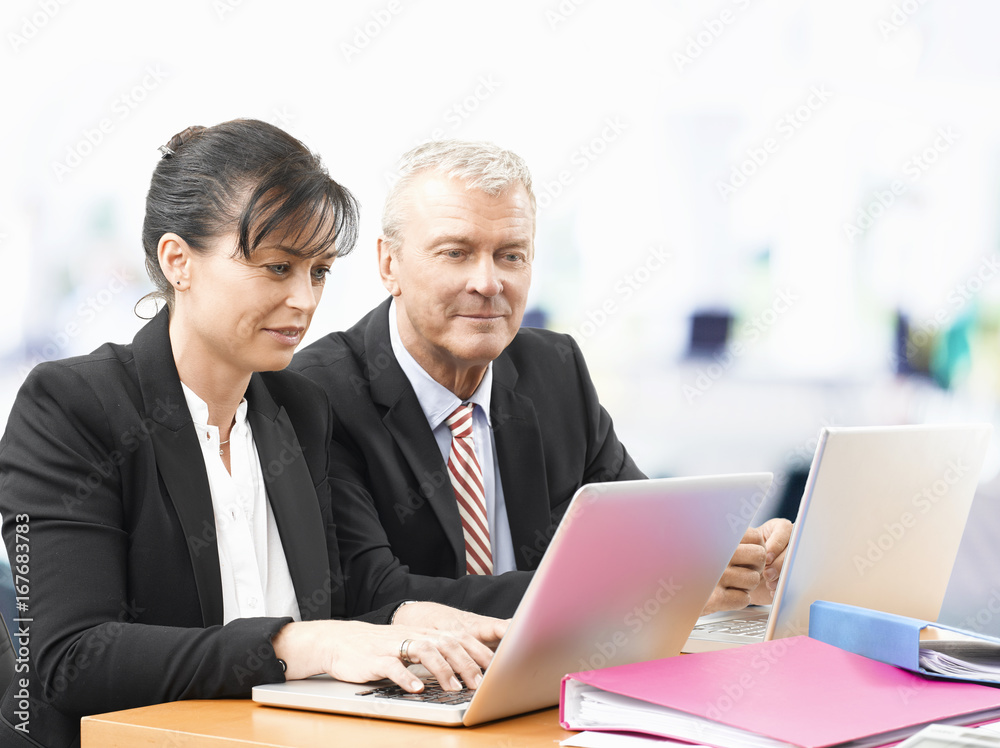 Business management. Shot of an senior investment advisor businessman and his female financial assistant analysing data while working on laptops. Business management. Shot of an senior investment advisor businessman and his female financial assistant analysing data while working on laptops.