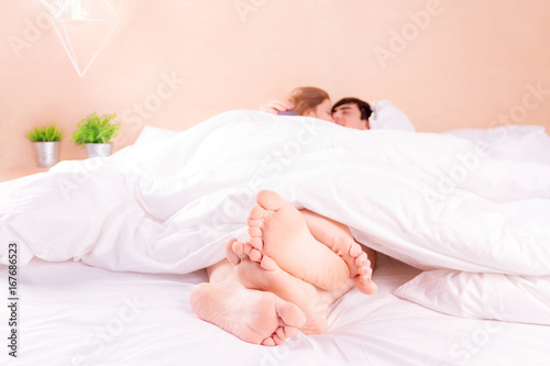 Couple in love man and woman in white bed in the morning. View on the foots