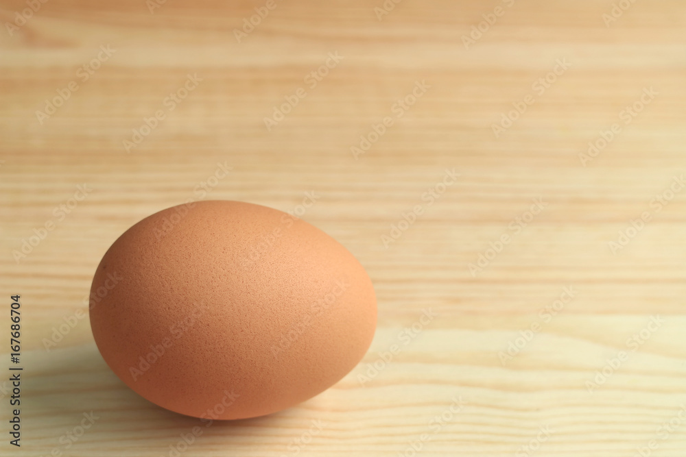 One fresh uncooked hen egg isolated on the wooden table, with free space for text and design 