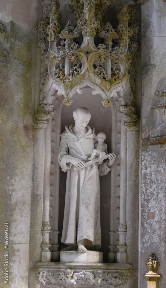 Detail in the park - old stone statue of monk with cross and baby, Quinta da Regaleira in Sintra, Portugal.