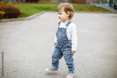 Cute baby girl with blonde hair running outdoors. Little girl 1-2 year old.