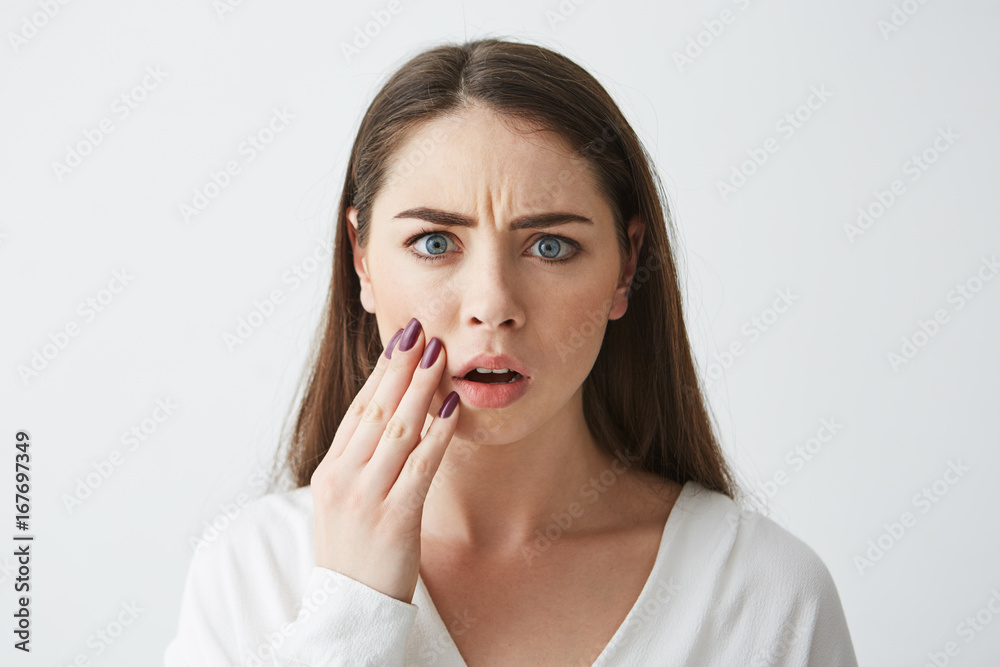 Close up photo of displeased frightened girl looking at camera touching face frowning over white background. Close up photo of displeased frightened girl looking at camera touching face frowning over white background.