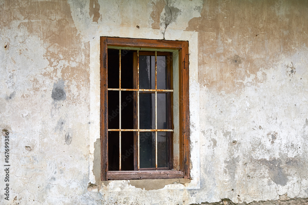 Old rotten window with rusty iron bars, missing the outer moving frames, in a ruined house facade