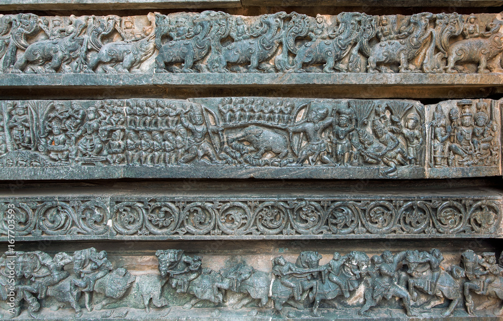 Hunting scene and other stone artworks on background sculptures on the Hindu temple. Mythical patterns of 12th century Hoysaleshwara temple in Halebidu, India
