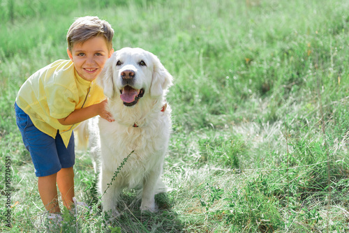 Cheerful boy hugging his dog on grass field