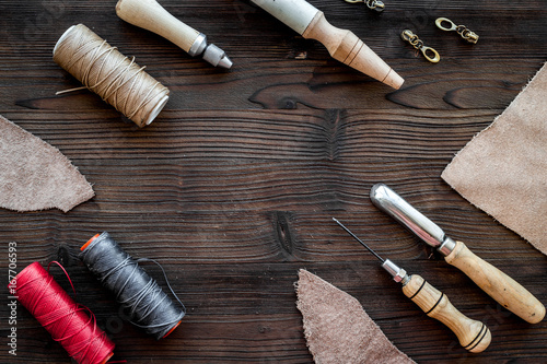 Leather craft. Knife, awl and other tools on dark wooden background top view copyspace