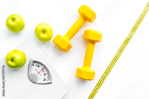 Sport and diet for losing weight. Bathroom scale, apple and dumbbell on white background top view