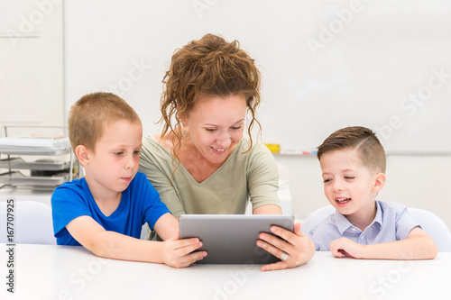 teacher woman using tablet computer with two preschooler boy in a classroom