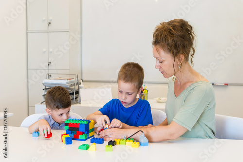 teacher woman play with two child boy with cubes in the kindergarten