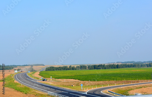 Beautiful gray empty asphalt country road into the distance with turns among the green fields against the blue sky on a sunny day, landscape