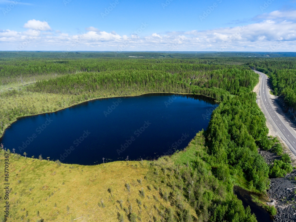 Fototapeta premium Aerial view at small forest lake, swamps and line of highway passing near. Northern Karelia, Russia