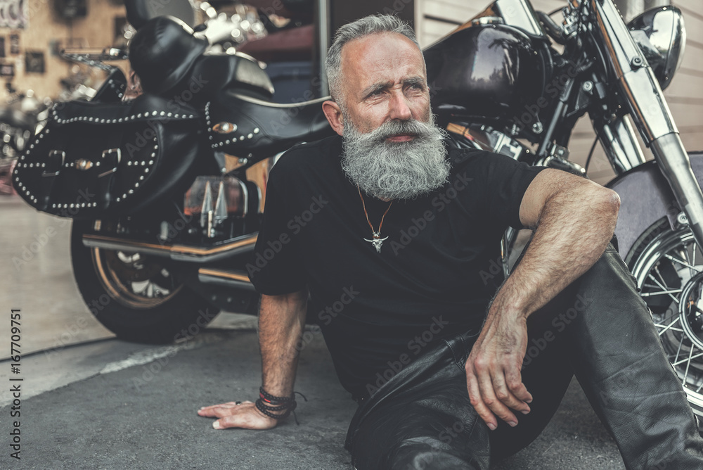 Fototapeta premium Marzycielski stary człowiek lokalizujący blisko motocyklu