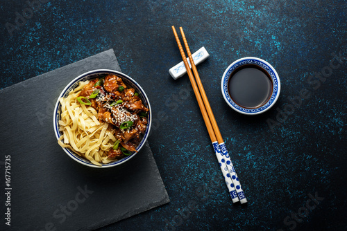 Chicken teriyaki on dark background with balsamic sauce and sesame seeds. Asian food. Noodles, chicken and soy sauce. Top view.