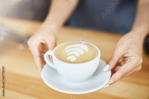 Close up of woman hands serving a cappuccino in a cup with latte art. Barista concept.