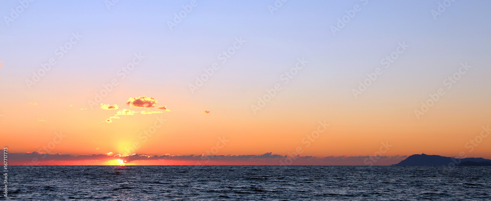 sunset behind clouds at the horizon over the sea