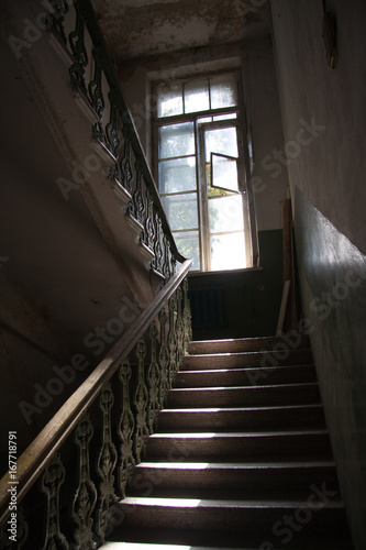 Dark vintage staircase interior in old building, stair with forged railing, big window with day light