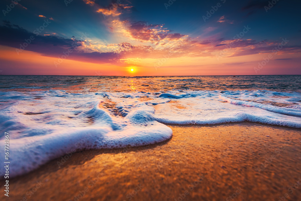 Beautiful sunrise over the sea and washing waves on the sand