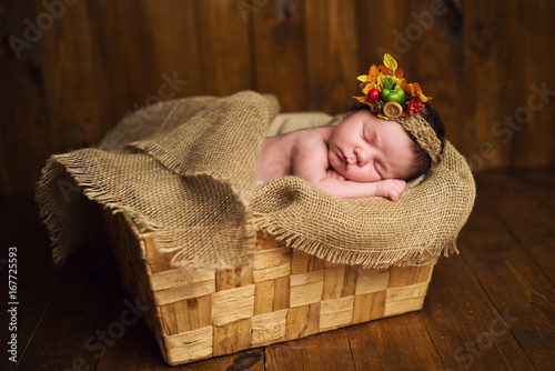 A cute newborn in a wreath of berries lies in a basket.