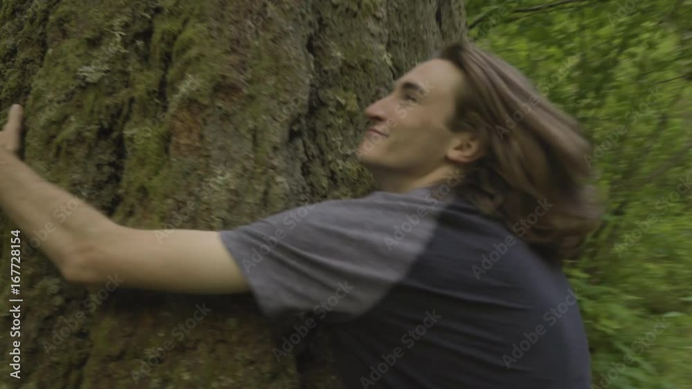 Steadicam Follow Shot Of Young Man Running On Nature Trail, He Stops And Hugs Giant Tree