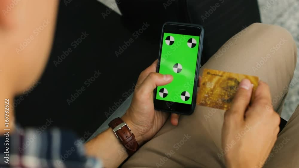 Young man shopping online with credit card using smart phone with green screen at the airport lounge. Indoor shot. Chroma key. Tracking motion. Young man shopping online with credit card using smart phone with green screen at the airport lounge. Indoor shot. Chroma key. Tracking motion.