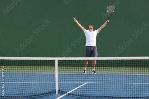 Tennis player man winning match happy excited with arms up in success on green outdoor court.