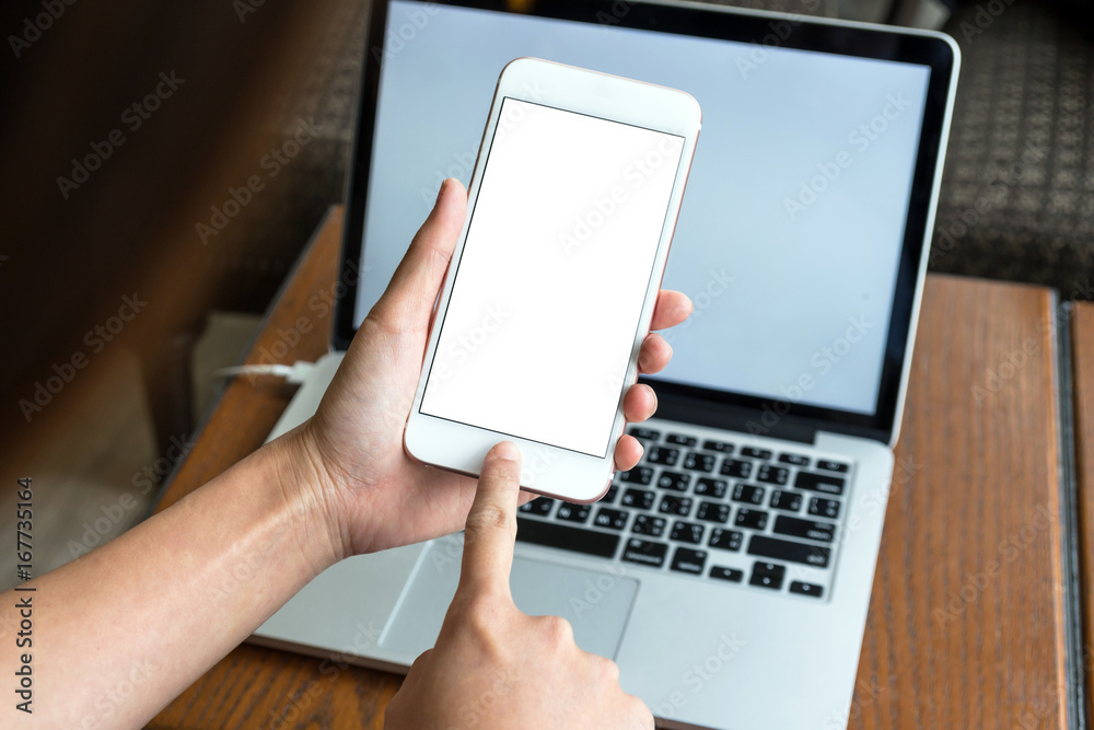 Hand holding the technology smart mobile phone shown white background for product mockup over the photo blurred of laptop with white background, business and technology concept Hand holding the technology smart mobile phone shown white background for product mockup over the photo blurred of laptop with white background, business and technology concept