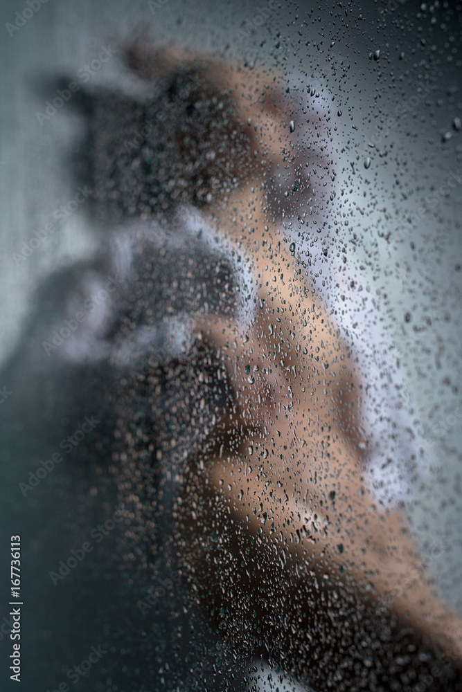 Beautiful woman in shower shot behind wet glass