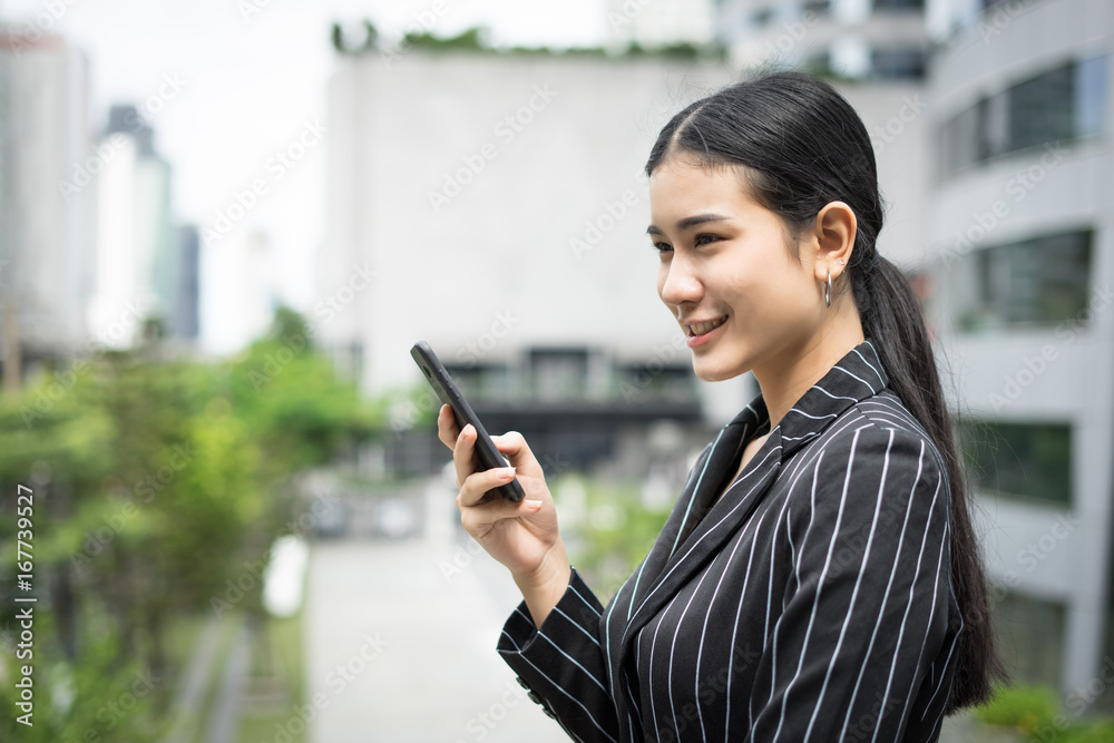 Young asian businesswoman using at mobile smartphone.Young female professional in the city in front of big building. Young asian businesswoman using at mobile smartphone.Young female professional in the city in front of big building.