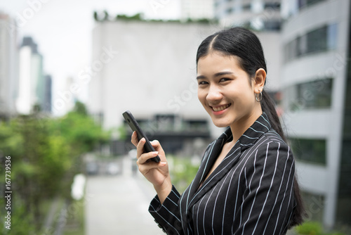 Young asian businesswoman using at mobile smartphone.Young female professional in the city in front of big building.