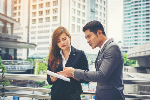 Business man pointing at document with smile and discussing something with her coworker while standing in front of office.