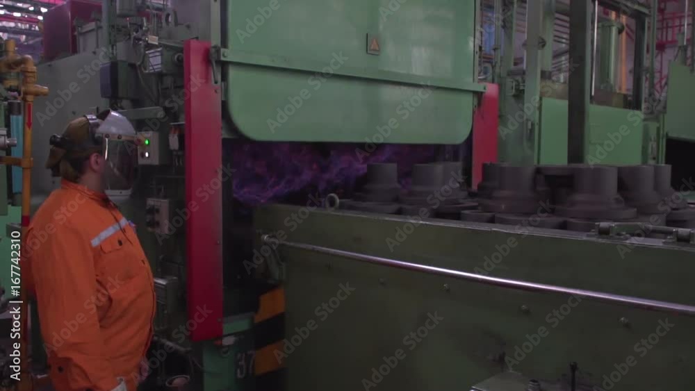 A worker in an orange suit opens the stove in a large factory, for tempering the parts.