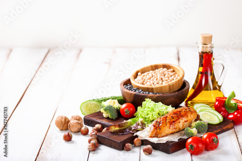The baked chicken fillet and vegetables. Healthy and fitness food. Meat, salad, vegetables, nuts, beans on a light wooden background. Selective focus. Copy space