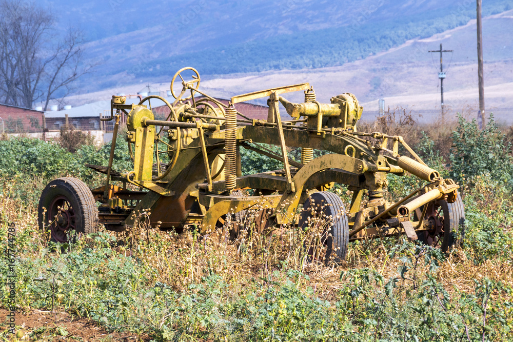 Fototapeta premium Vintage Yellow Farm Implement Against Rural Farm Landscape